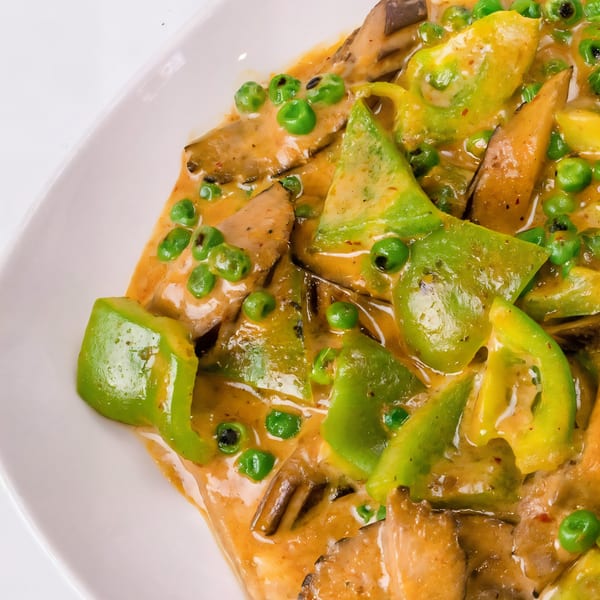 Close-up of Thai curry with green bell peppers, peas, and mushrooms in a rich orange sauce.