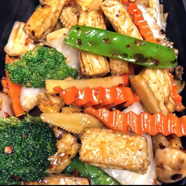 Close-up of Thai stir-fried vegetables and tofu, including broccoli, carrots, and snap peas.